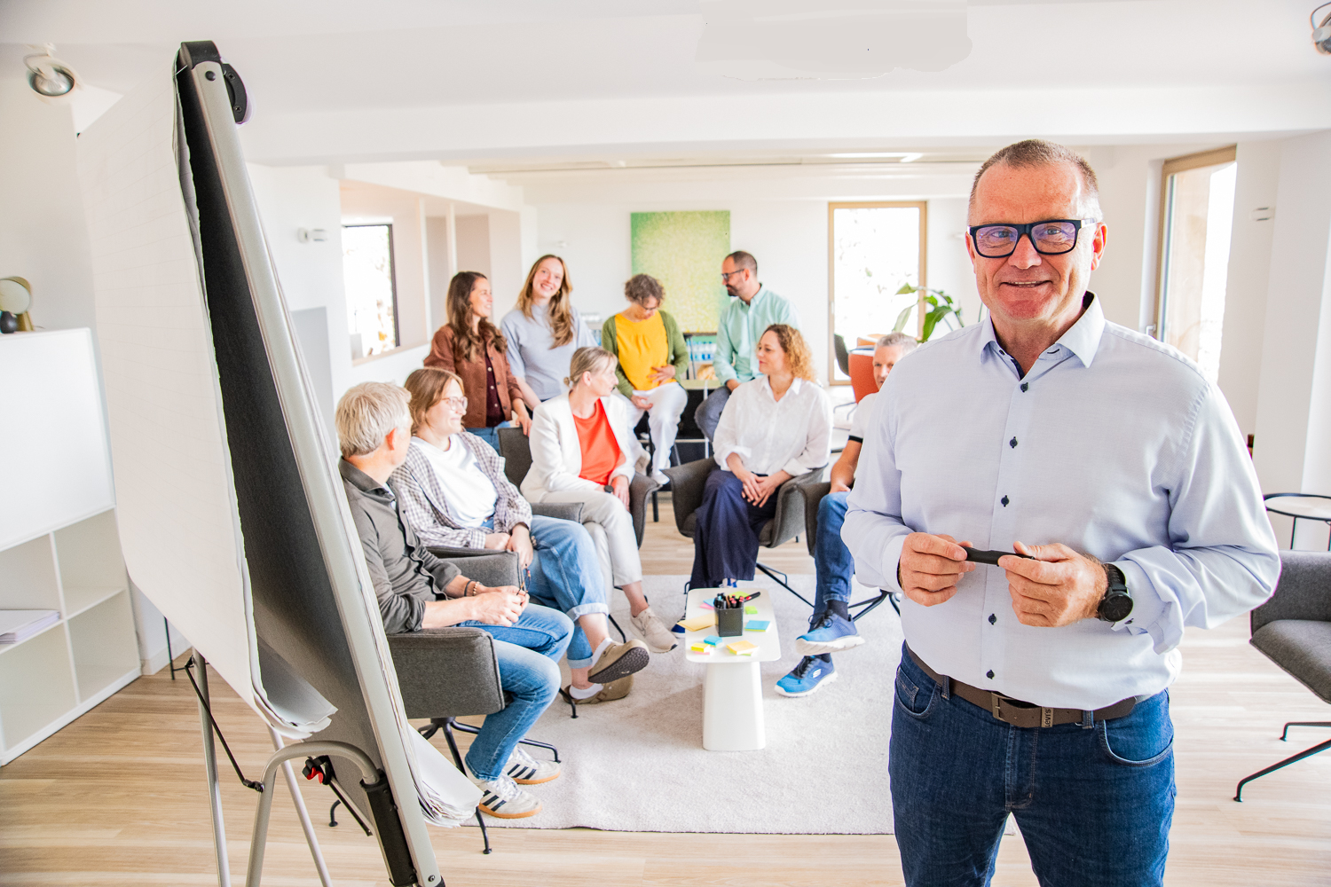 Dirk Beiser moderiert einen Teamworkshop am Flipchart, im Hintergrund die Gruppe im Gespräch